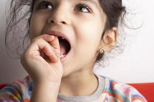 Little girl portrait trying to remove loose milk-tooth photo