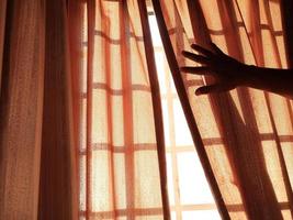 A cropped hand sliding the curtain to let in the morning light photo