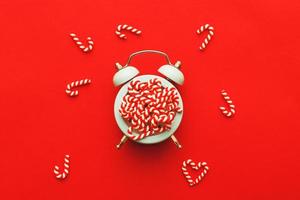 Christmas background with candy canes on alarm clock on red background photo