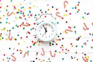 Christmas background with candy canes with alarm clock and multicolored sequins on wooden background photo