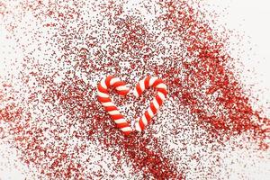 Christmas composition with candy canes in form oh heart on blue wooden background with red sequins photo