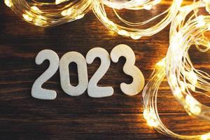 wooden number 2023 on christmas shiny wooden background. with sparkle festive gold garland photo