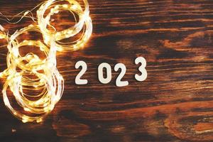 wooden number 2023 on christmas shiny wooden background. with sparkle festive gold garland photo