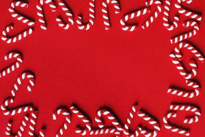Flat lay Christmas composition with frame of candy canes on a red background. Copy space for text photo