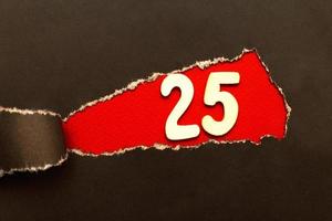 curl of torn black paper on red background with wooden number 25 photo