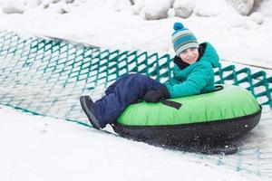 niño divirtiéndose en el tubo de nieve. chico está montando un tubo. entretenimiento de invierno. niño deslizándose cuesta abajo en el tubo foto