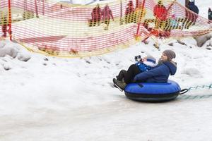 familia divirtiéndose en el tubo de nieve. madre con hijo está montando un tubo. gente deslizándose cuesta abajo en el tubo foto