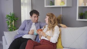 The mother is talking and chatting with her son at home. Mother and son sitting on the sofa and chatting with coffee cups in their hands. video