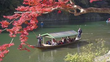 23/11/2019 quioto, japão. rio arashiyama colorido, com barco turístico na água e floresta nas margens do rio em cores de outono video