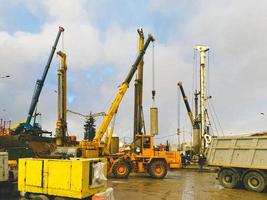 equipo de construcción en el sitio de reparación del paso elevado. una grúa metálica alta y amarilla lleva un bloque de hormigón redondo, una pila para la construcción de un gran paso elevado foto