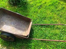 una carretilla de metal para transportar productos y fertilizantes se encuentra sobre la hierba verde. una carretilla para trabajos de jardinería. jardinero, inventario de jardinero. cuidado del jardín foto