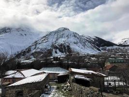 Small stone houses, buildings in the village on a beautiful mountain cold winter resort with high mountain peaks mist and snow covered rocks for snowboarding and skiing against a blue sky photo