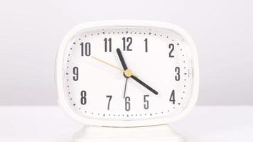 Front view of a clock that rotates with time placed on a white table. video