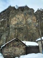 Small stone houses, buildings in the village on a beautiful mountain cold winter resort with high mountain peaks mist and snow covered rocks for snowboarding and skiing against a blue sky photo