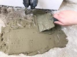 Builder hands with a metal spatula plaster the wall, pours the screed with plaster, tile glue, cement for the repair of the apartment, building a house, leveling the walls and pouring photo