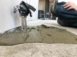 manos constructoras con una espátula de metal enyesan la pared, vierten la regla con yeso, pegamento para azulejos, cemento para la reparación del apartamento, construyen una casa, nivelan las paredes y vierten foto