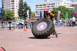 A fireman in a fireproof suit and a helmet runs and turns a large rubber wheel in a fire fighting competition, Belarus, Minsk, 08.08.2018 photo