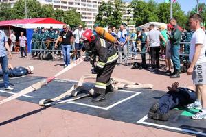 A fireman in a fireproof suit and a helmet running with an oxygen balloon pulling, holding a fire hose at a fire sport competition. Minsk, Belarus, 08.07.2018 photo