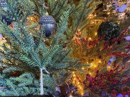 Green branches of a fluffy Christmas festive New Year tree with toys in balls and bright glowing light bulbs and garlands, background photo