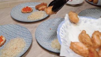 la mano de una mujer coloca pescado frito en platos sobre la mesa de la cocina. video