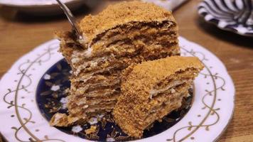 A multi-layered sweet cake in a plate on the table is eaten with a spoon. video