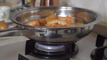 Deep-fried fish is cooked in a metal skillet standing on a gas stove. video