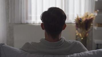 gelukkig Mens is resting en genieten van Bij huis. de Mens zittend Aan de sofa zet zijn handen Aan zijn hoofd en rust, ontspant. video