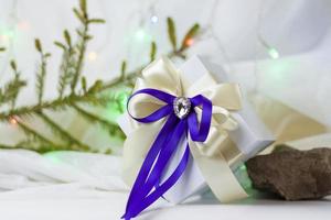 A Christmas gift decorated with a beautiful bow on a light background with a twig, if. Selective focus. the concept of Christmas and New Year. photo