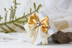 A Christmas gift decorated with a beautiful bow on a light background with a twig, if. Selective focus. the concept of Christmas and New Year. photo
