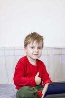 A cute boy is on the bed looking at a tablet. Online training, communication on the Internet. Funny smiling child. photo