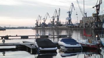 kleine motorboote angedockt am rigaer freihafen entlang des flusses daugava in riga, lettland. Hafenkräne und Containerterminal im Hintergrund. video