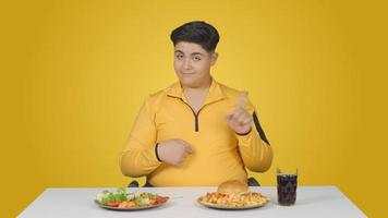 criança obesa, problema de peso. escolha alimentar saudável. menino obeso escolhendo entre salada e hambúrguer. video