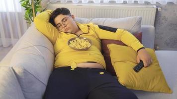 fetma den där falls sovande med mat är ung. ung föll sovande medan tittar på tv. han är fick en tallrik av pommes frites på hans knä. video