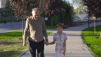 Grandfather is taking his grandson for a walk. Grandfather and grandchild walking outdoors. video