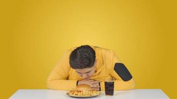 obeso ragazzo annusando un' Hamburger. sovrappeso ragazzo annusando e simpatia il Hamburger su il tavolo video