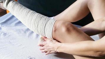 femme après une chirurgie du genou mettant un bandage sur le canapé. femme portant une orthèse de genou ou une attelle de soutien du genou après une intervention chirurgicale sur la vue de face de la jambe video