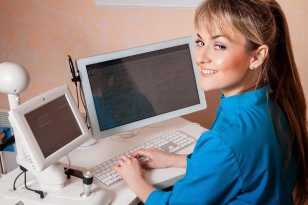 Female Doctor working in a cabinet at the computer and smiling