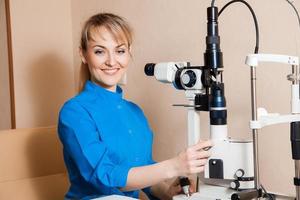 Happy young beautiful Doctor at work machine for checking vision photo