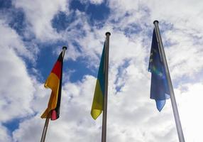 Flags of Ukraine, Germany and European Union fly side by side against blue sky. photo