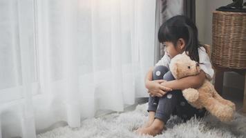 Close up lonely little girl hugging toy, sitting at home alone, upset unhappy child waiting for parents, thinking about problems, bad relationship in family, psychological trauma photo