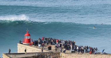 människor tittar på de stor jätte vågor kraschar nära de fort av nazare fyr i nazare, portugal. största vågor i de värld. turistiska destination för surfing och älskande av radikal sporter. video