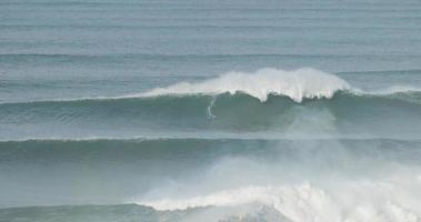 le surfeur surfe sur une grosse vague géante à nazare, au portugal. plus grosses vagues du monde. destination touristique pour le surf et les amateurs de sports radicaux. jet-skis dans l'eau. des destinations incroyables. video