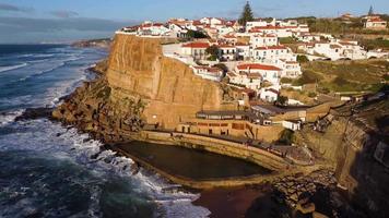 vista aérea drone de uma piscina natural no oceano, junto à falésia e uma vila à beira-mar durante o pôr do sol. Azenhas do Mar, Portugal. melhores destinos do mundo. lugares mais visitados. feriados. video