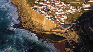 Aerial drone view of a natural pool in the ocean, next to the cliff and a seaside village during sunset. Azenhas do Mar, Portugal. Best destinations in the world. Most visited places. Holidays.