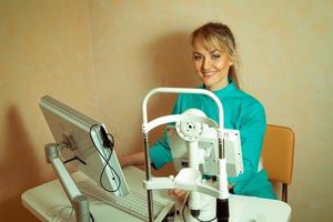 Ophthalmologist beautiful blonde working at the computer and smiling at the camera photo