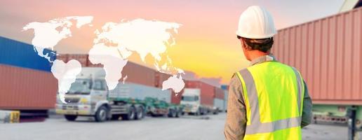 A truck driver wearing a helmet stands in a parking lot. photo