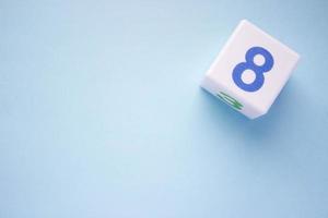 Close-up photo of a white plastic cube with a blue number 8 on a blue background in the upper right corner. With copy space