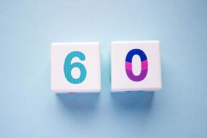 Close-up photo of a white plastic cubes with a colorful number 60 on a blue background. Object in the center of the photo