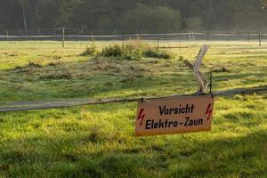 Meadow with warning sign caution electric fence photo