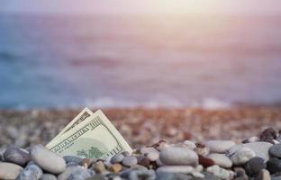 Hundred dollars half covered with round rocks lie on beach photo